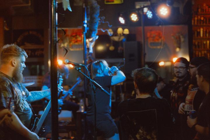 A band performs on a dimly lit stage with colorful lights.