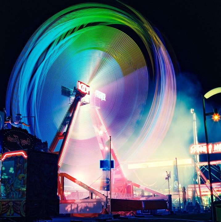 A long exposure photograph captures the colorful light trails of a spinning amusement park ride at night.