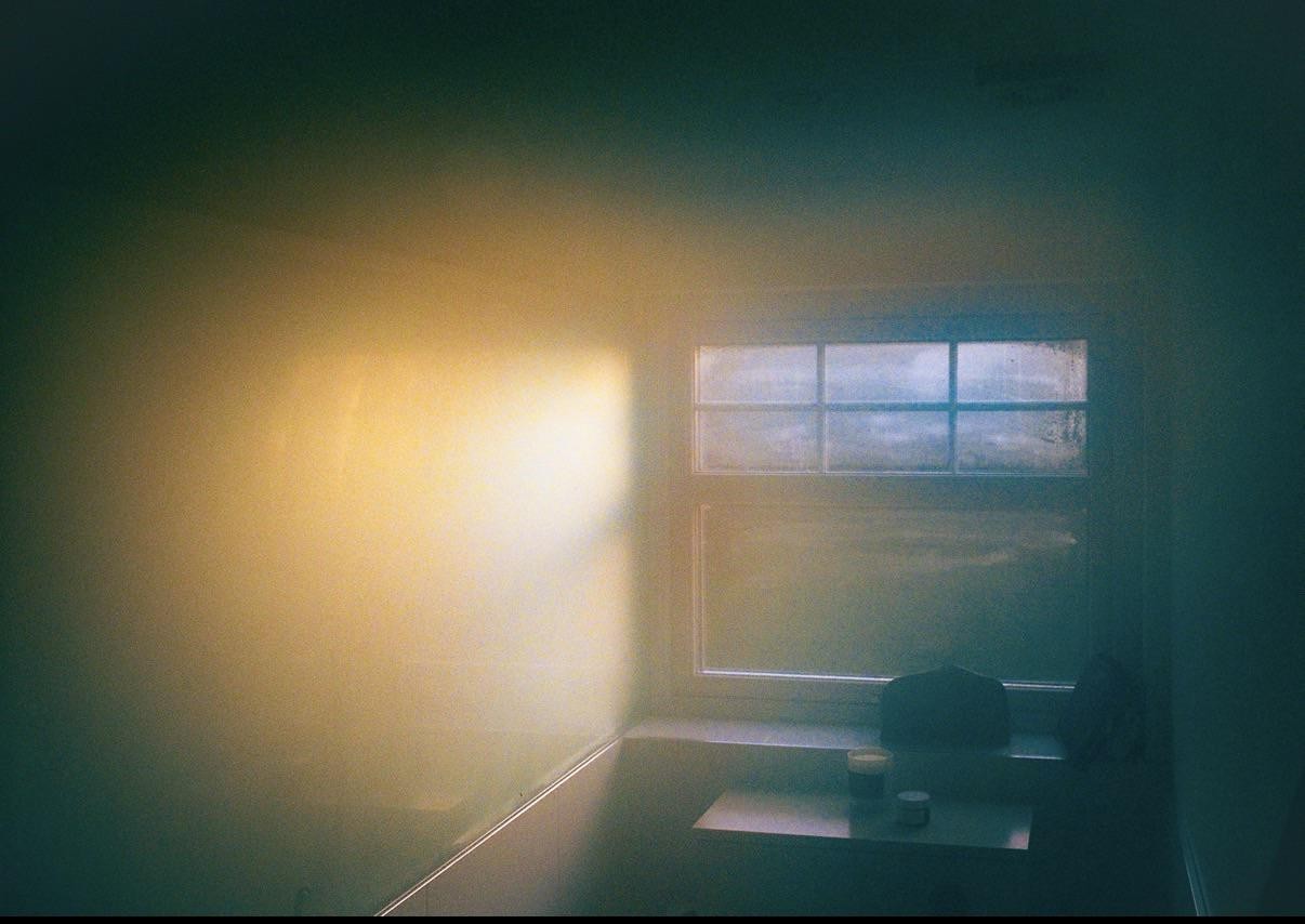 Sunlight streams through a window onto a wall and a small table with two containers.