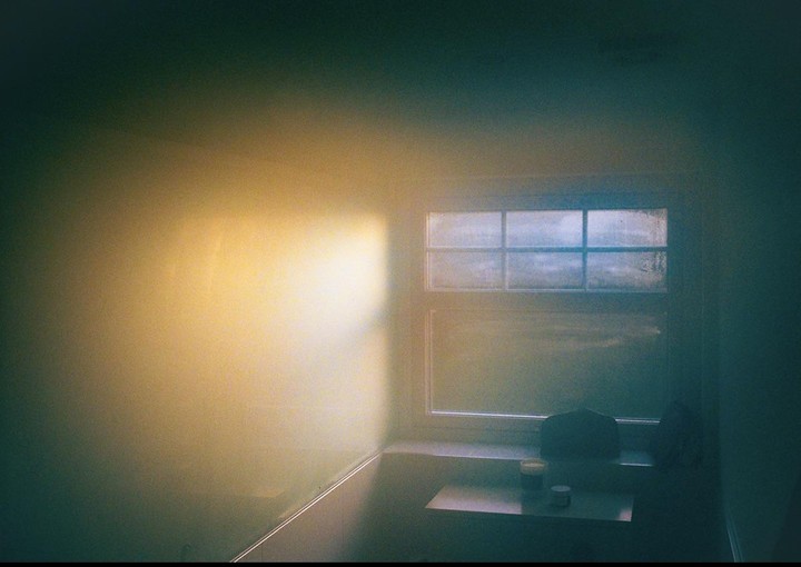 Sunlight streams through a window onto a wall and a small table with two containers.
