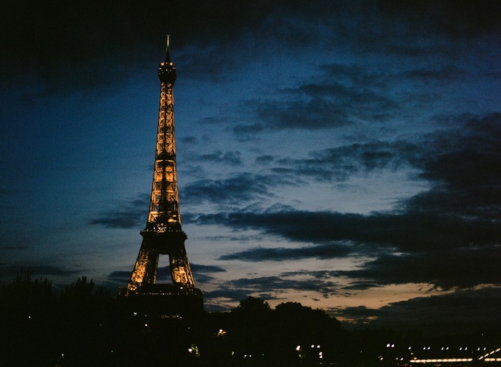The Eiffel Tower is illuminated against a dark, cloudy sky at dusk.