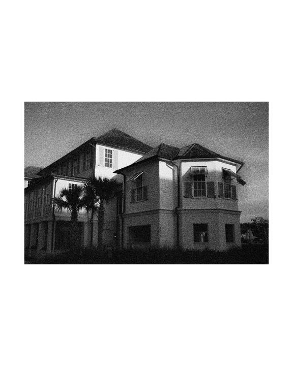 A large house with multiple windows and palm trees in front is captured in black and white.