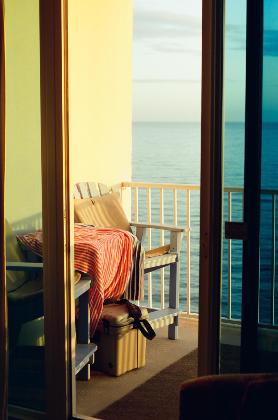 A balcony with chairs and a cooler overlooks the ocean at sunset.