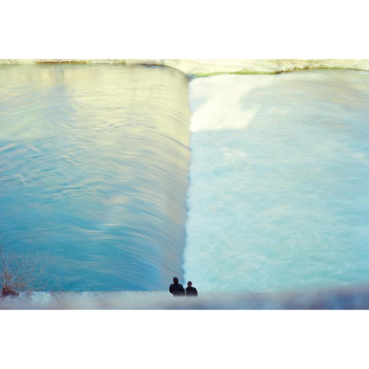 Two people sit on a wall looking at a waterfall with a long exposure.