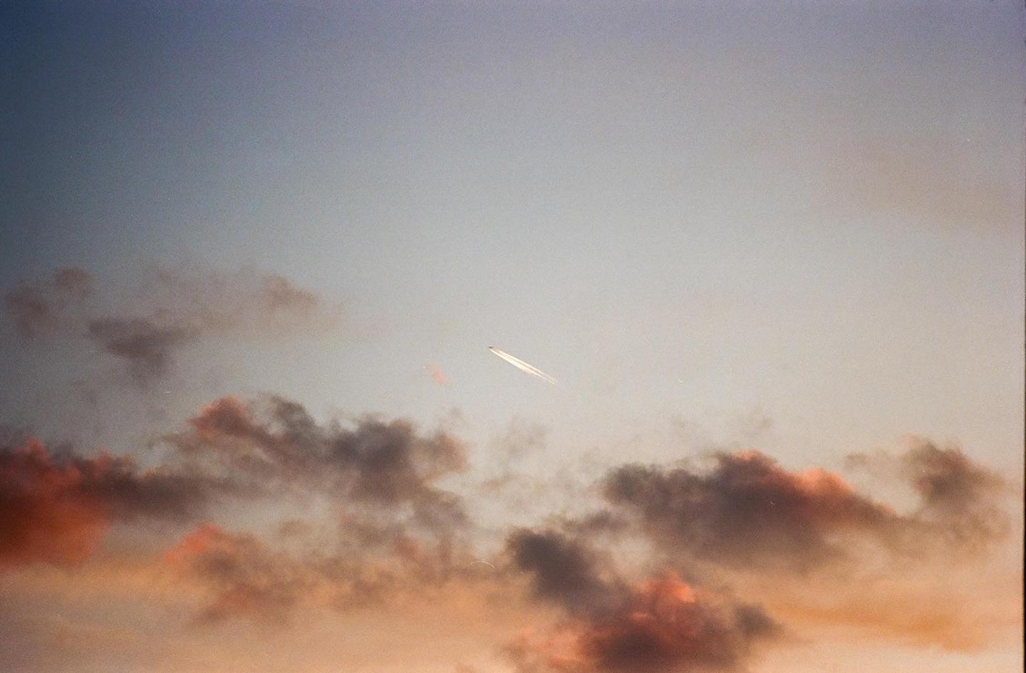 A jet airplane with a contrail flies across a sky with clouds at sunset.