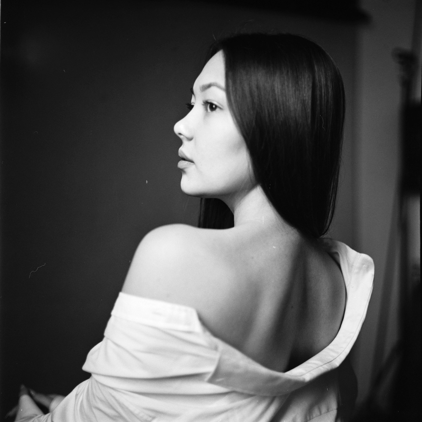 A woman with long hair looks to the right, her back to the viewer, wearing a white shirt off her shoulders.