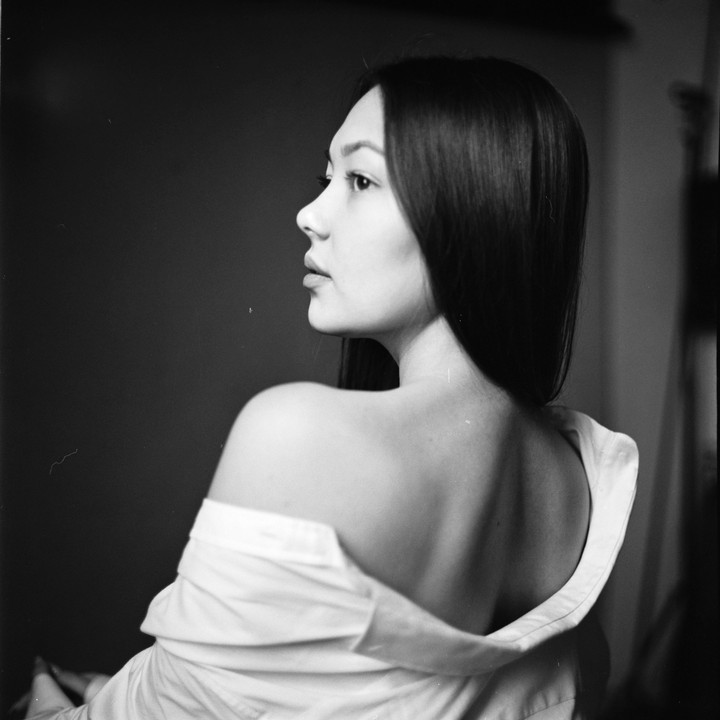 A woman with long hair looks to the right, her back to the viewer, wearing a white shirt off her shoulders.