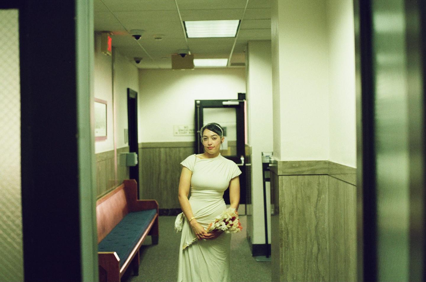 A woman in a white dress holds a bouquet of flowers while standing in a hallway.