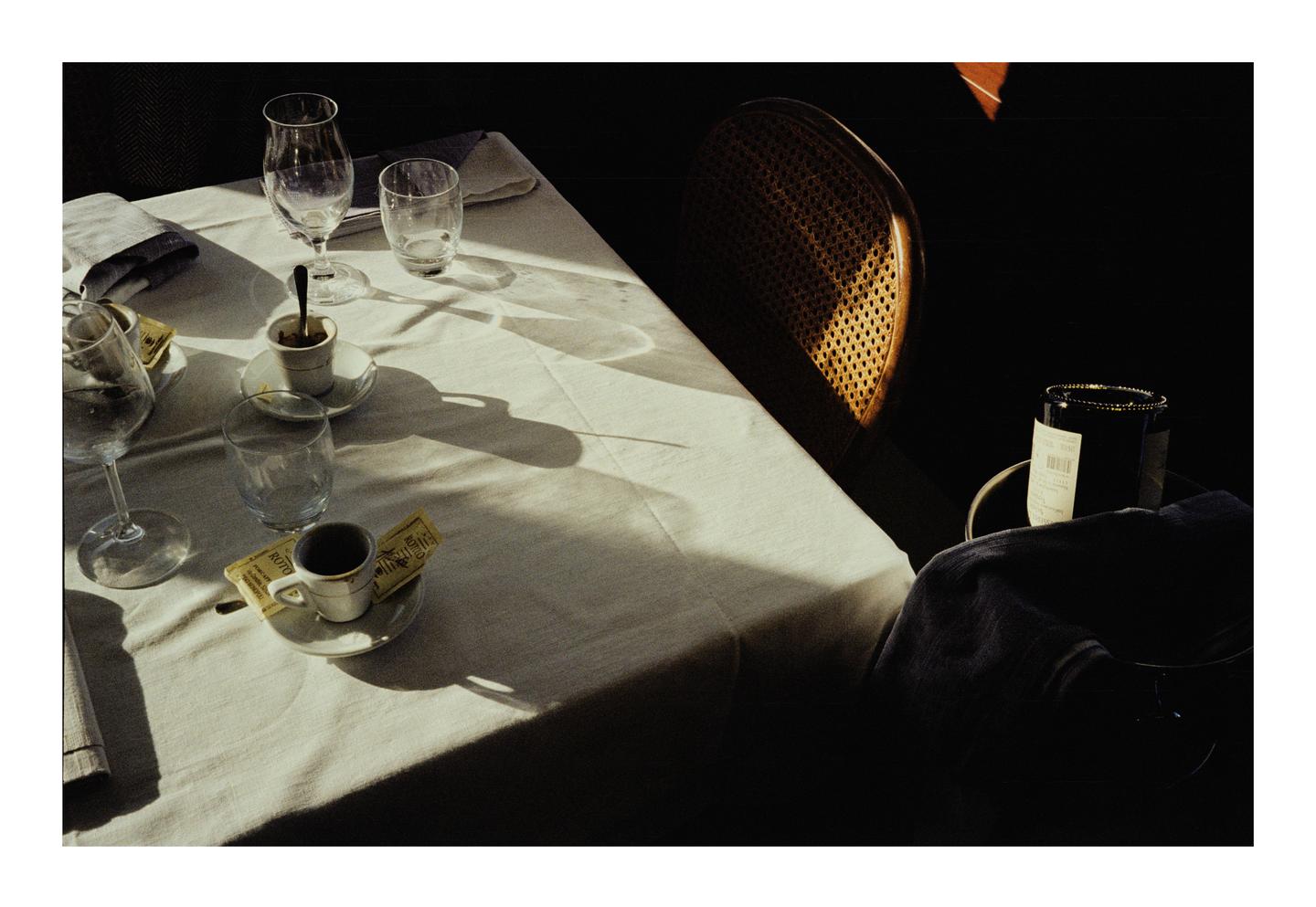 A table set with cups, glasses, and a bottle of wine is illuminated by a shaft of sunlight.