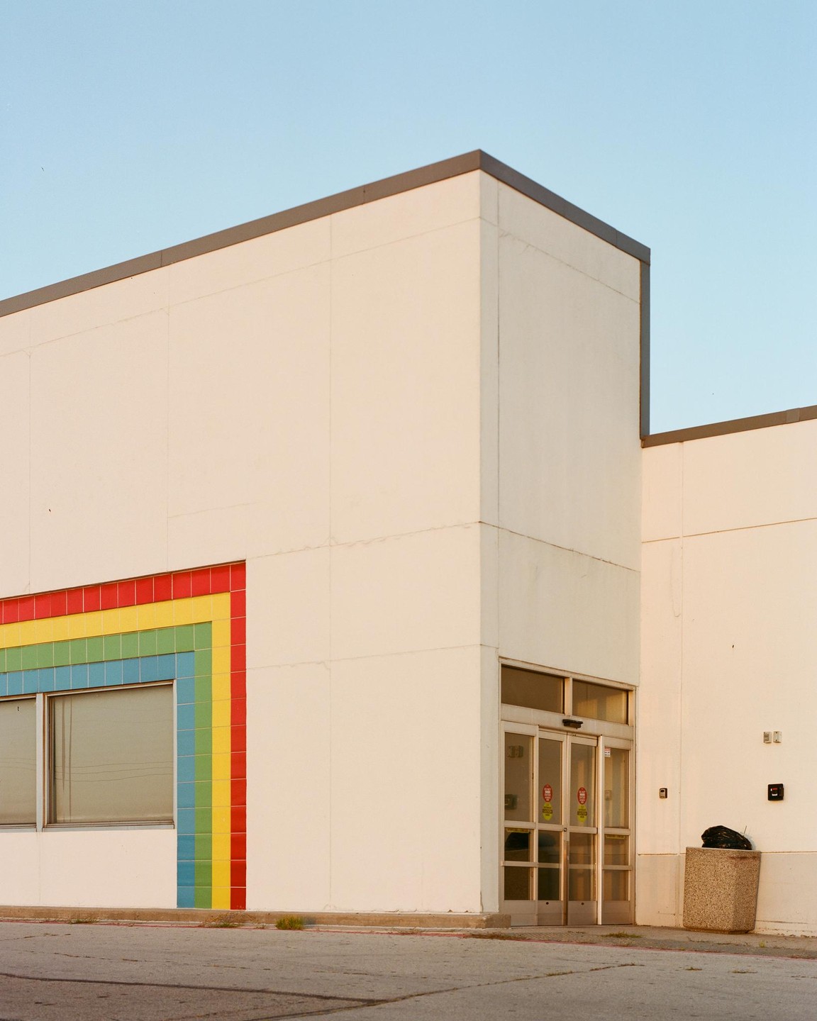A white building with a rainbow-colored tiled wall and an automatic door is shown under a clear sky.