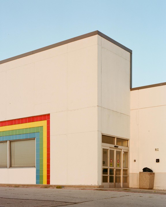 A white building with a rainbow-colored tiled wall and an automatic door is shown under a clear sky.