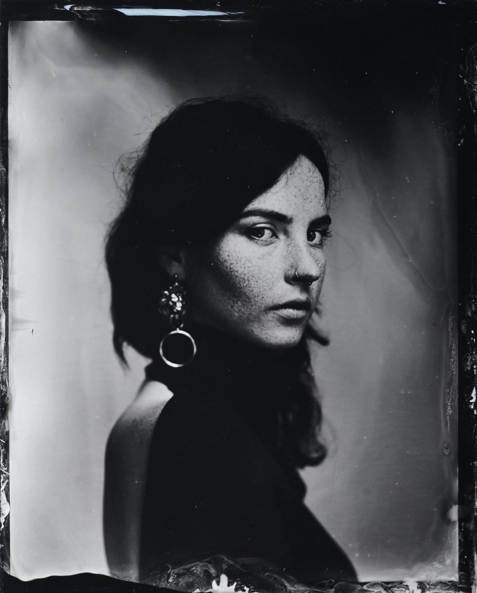 A woman with dark hair and freckles looks over her shoulder at the viewer.