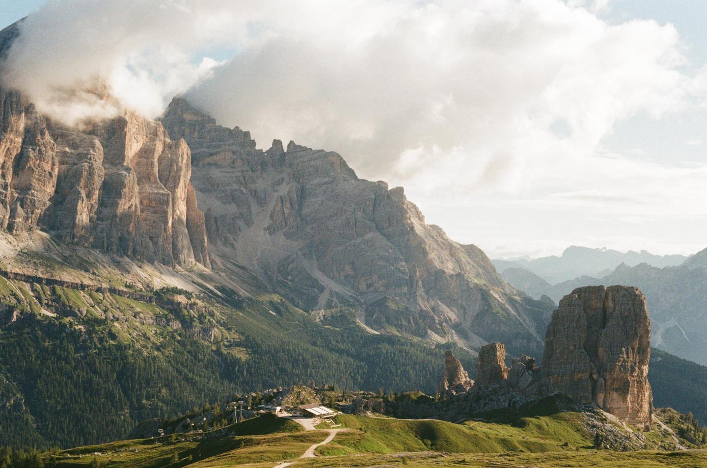 Clouds partially obscure the peaks of the Dolomites, with a small building nestled in the valley below.
