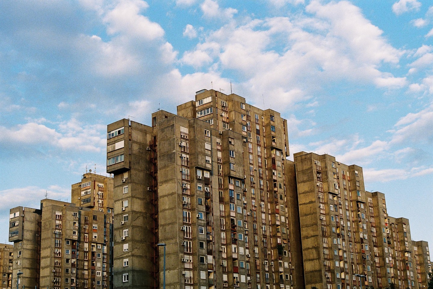 A cluster of brutalist apartment buildings stands under a partly cloudy sky.