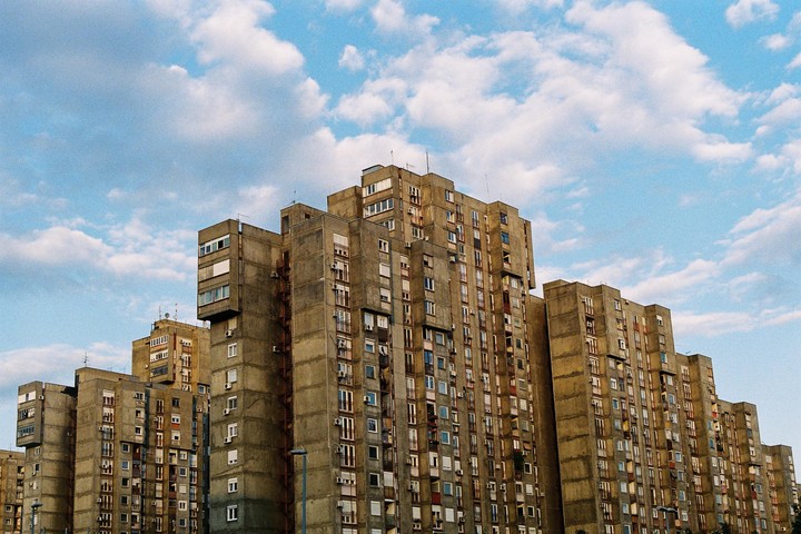 A cluster of brutalist apartment buildings stands under a partly cloudy sky.