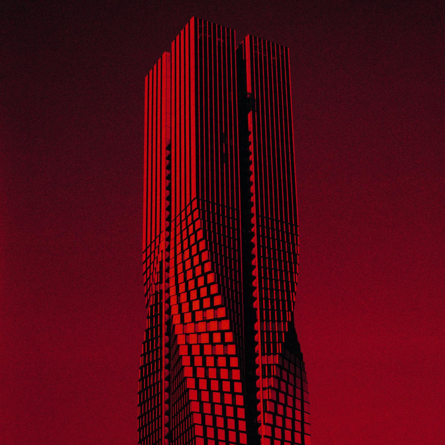 A tall, modern building with a red facade stands against a red sky.