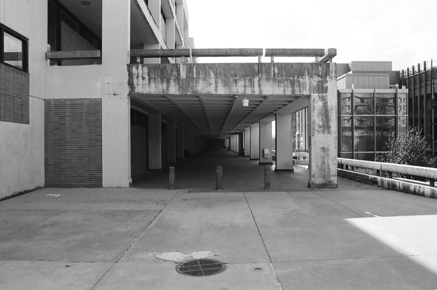 A long, dark, covered walkway extends into the distance between two buildings, with a drain cover in the foreground.