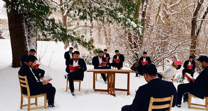 A group of men in suits are sitting on chairs in a snowy forest, reading books.