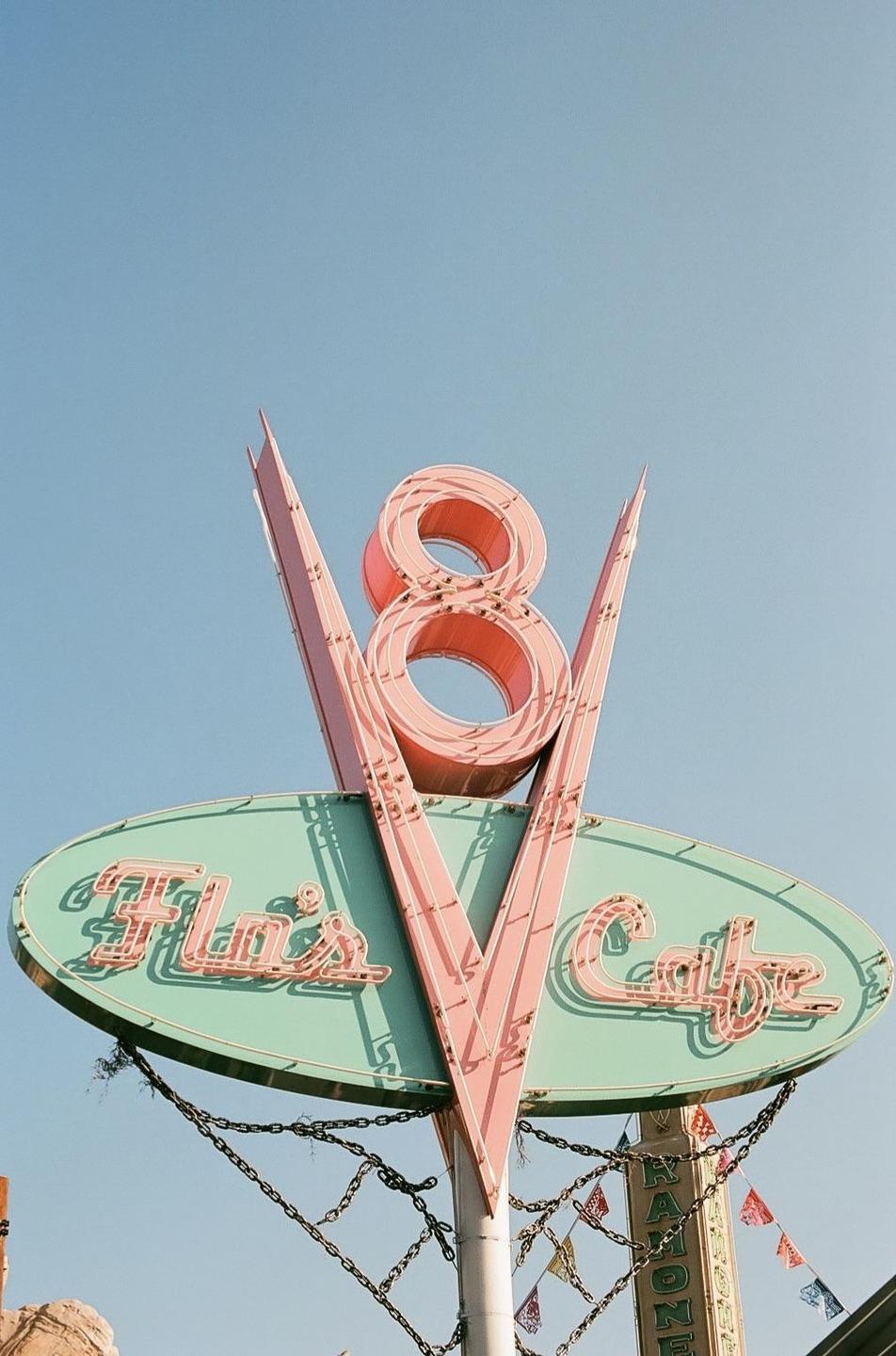 A neon sign for Flo's V8 Cafe is set against a clear blue sky.