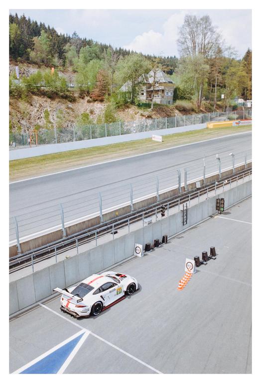 A white race car with red stripes is parked on a race track next to orange traffic cones.