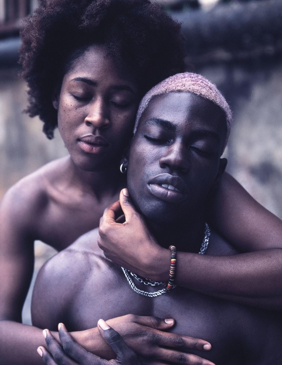 A woman embraces a man from behind, both with their eyes closed.
