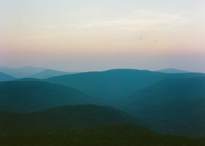 A landscape view shows multiple layers of mountains under a colorful sky.