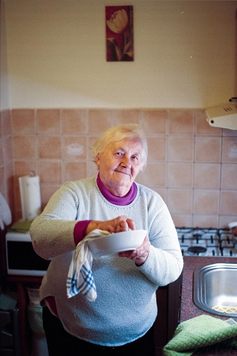 A woman smiles at the camera while drying a bowl in a kitchen.