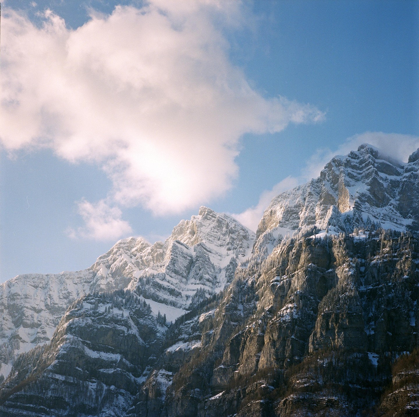 Snow-covered mountains are illuminated by late afternoon light under a blue sky with white clouds.