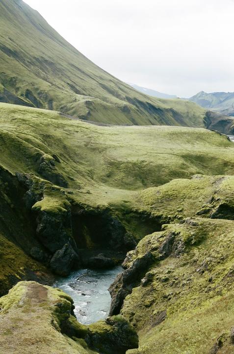A river flows through a green, mossy canyon surrounded by hills.