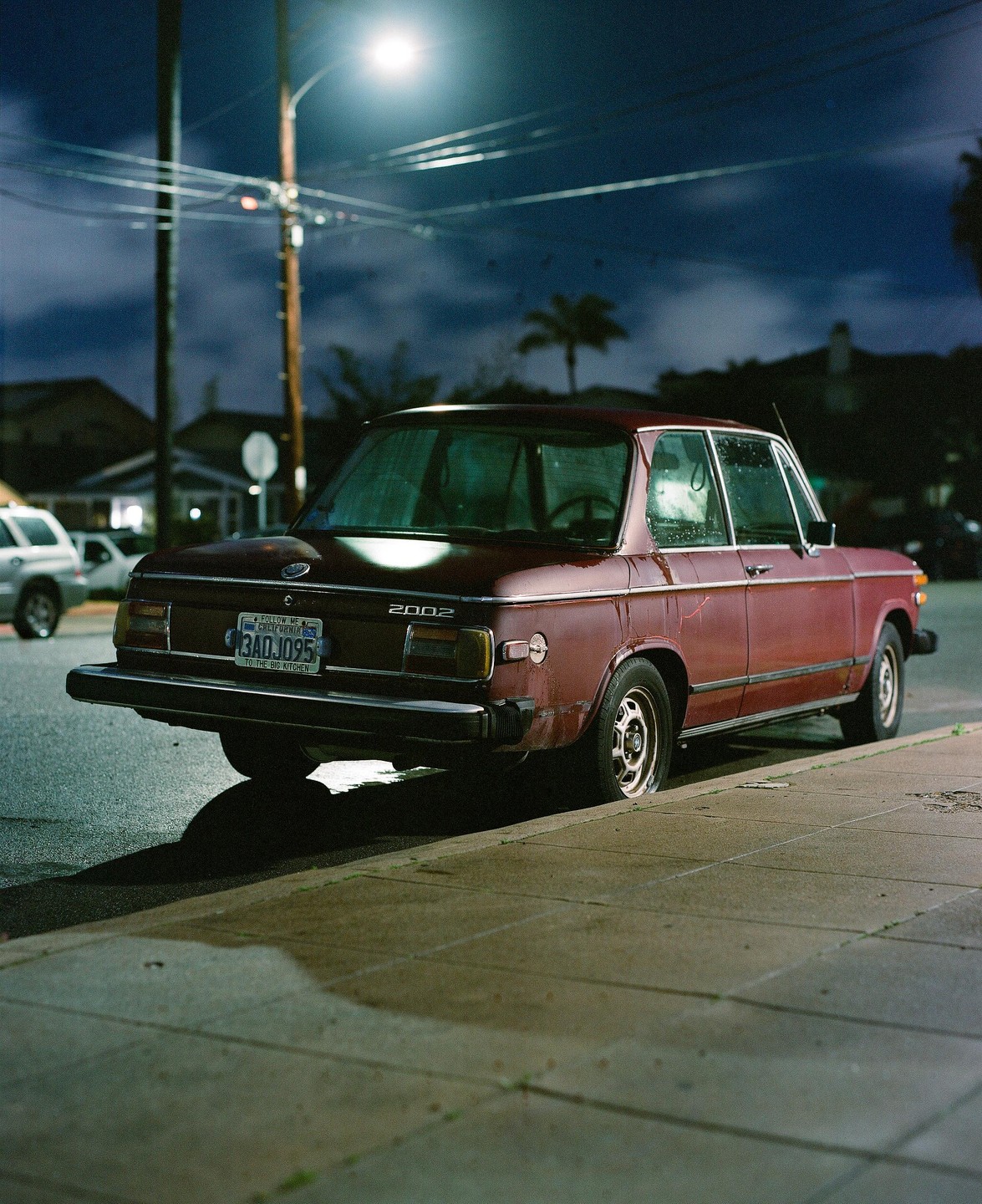 A red car is parked on the side of a street at night under a street light.