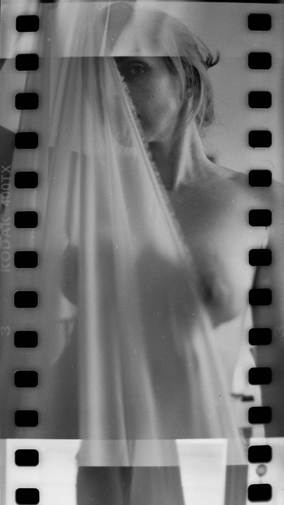 A woman is partially obscured by a sheer fabric, with one eye visible.