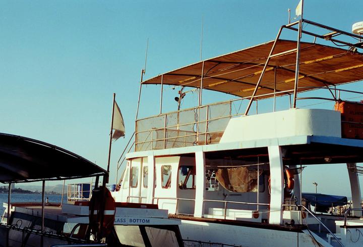 A white boat with a canvas canopy is docked in a harbor under a clear blue sky.