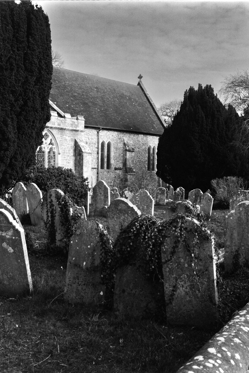 A stone church with a tall roof stands behind a graveyard filled with old, weathered tombstones.