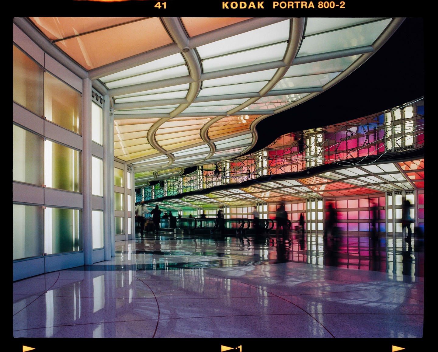 People walk through a long tunnel with a colorful, illuminated ceiling and walls.