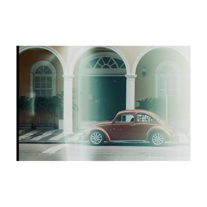 A red beetle car is parked in front of a building with arches and columns.