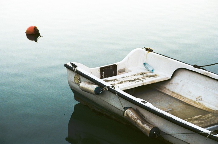 A small white boat with a red buoy in the water.