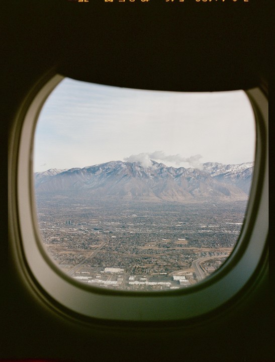 A view from an airplane window shows a city with mountains in the background.