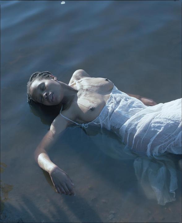 A woman in a white dress floats on her back in dark water.