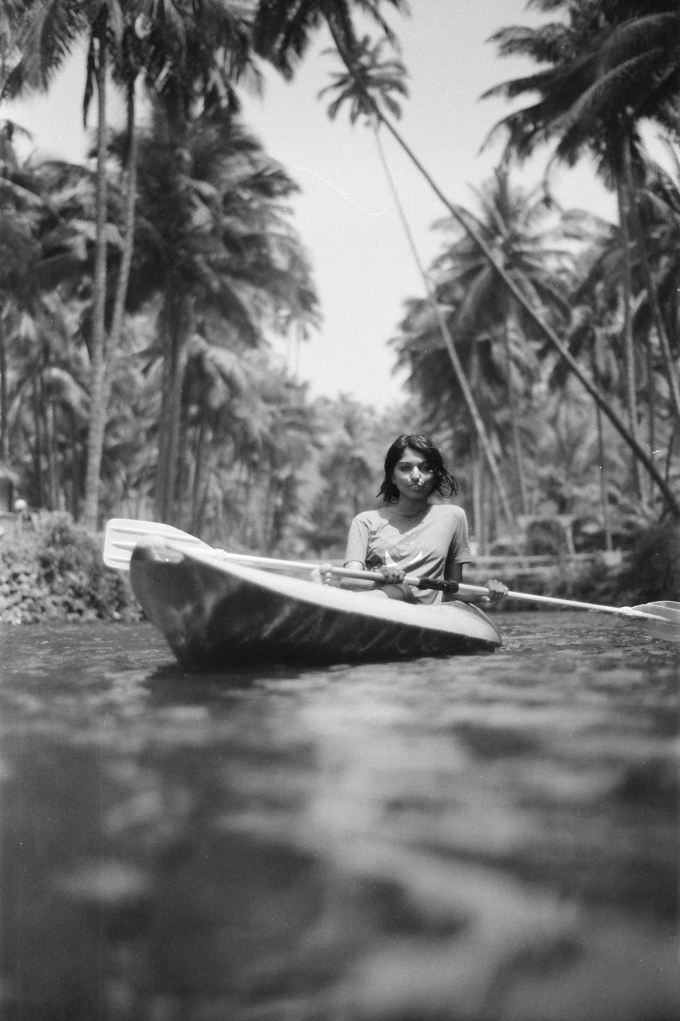 A woman in a kayak paddles through water surrounded by palm trees.