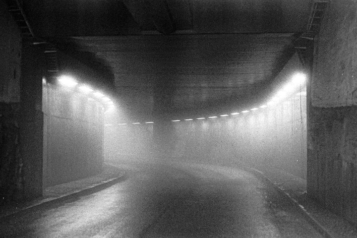 A curving tunnel is illuminated by lights along its walls, with a hazy atmosphere.