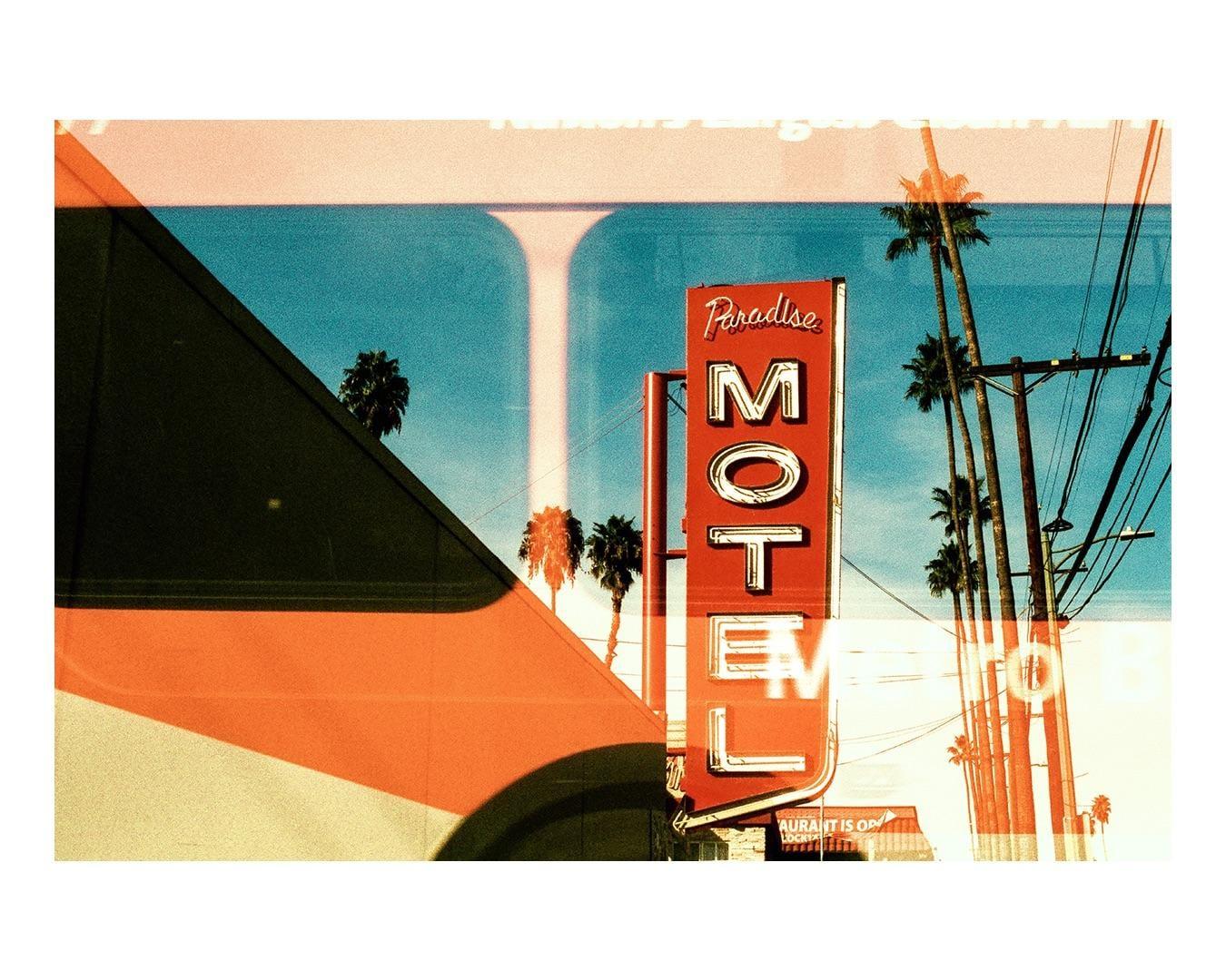 A red motel sign with "Paradise Motel" written on it stands against a blue sky with palm trees and power lines.