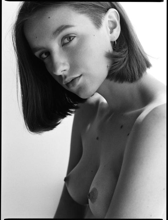 A woman with short hair and bare shoulders looks directly at the viewer.