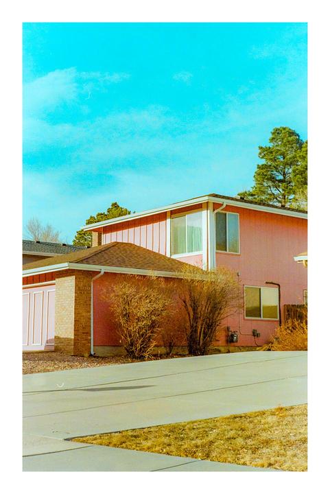A pink house with a brown roof and a garage is visible under a bright blue sky.