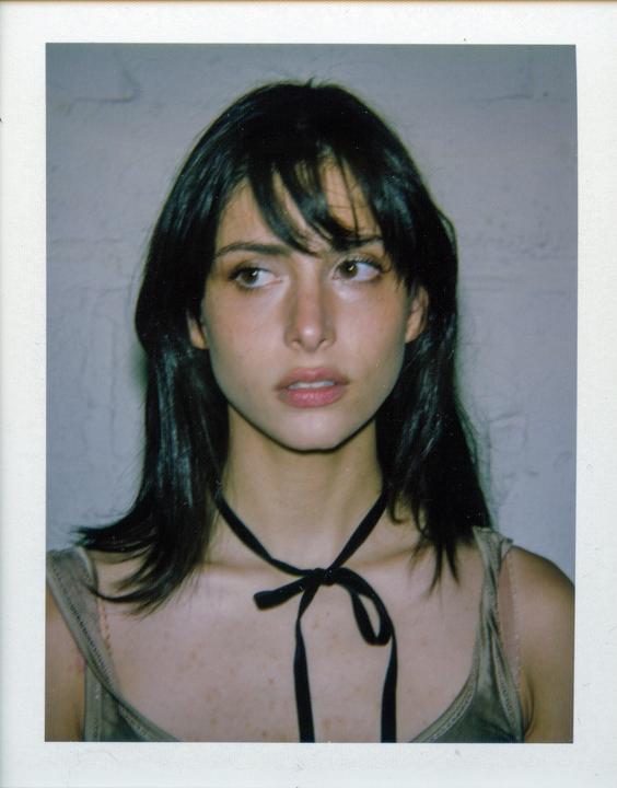 A woman with dark hair and a black ribbon around her neck looks to the right.