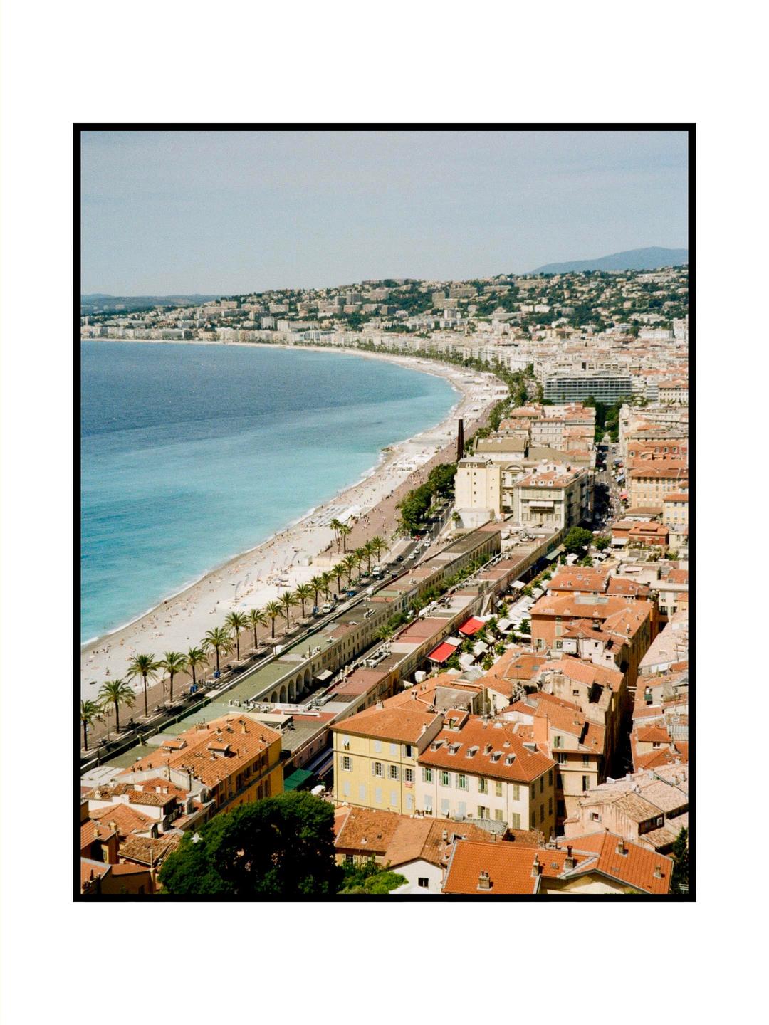 An elevated view shows a city with buildings and a beach along a curved coastline.