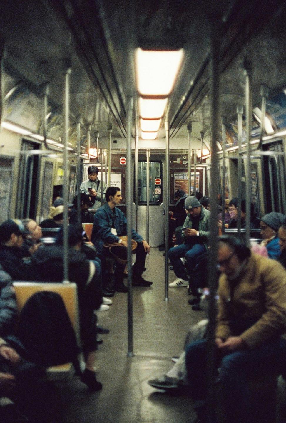 People are sitting and standing inside a subway car.
