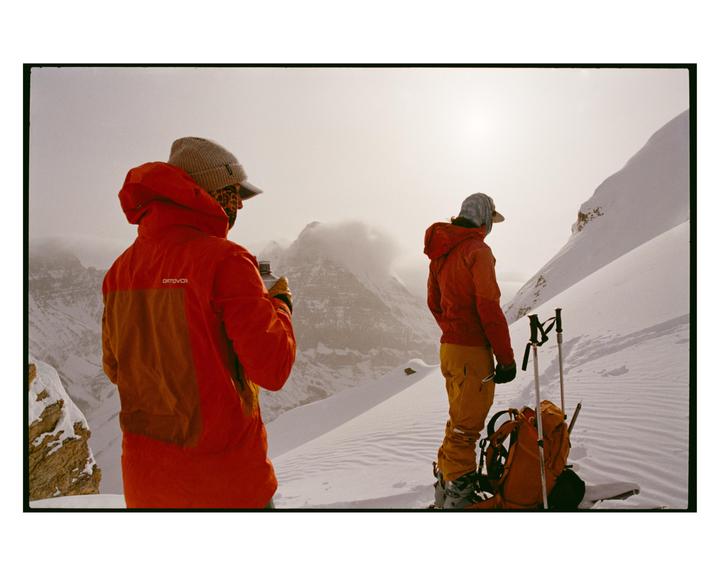 Two people stand on a snow-covered mountain with ski equipment.
