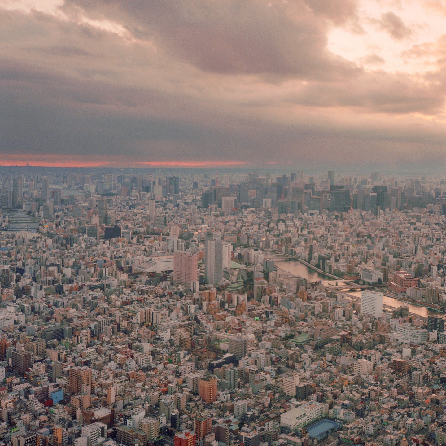 An aerial view shows a sprawling city under a cloudy sky with a hint of sunset.