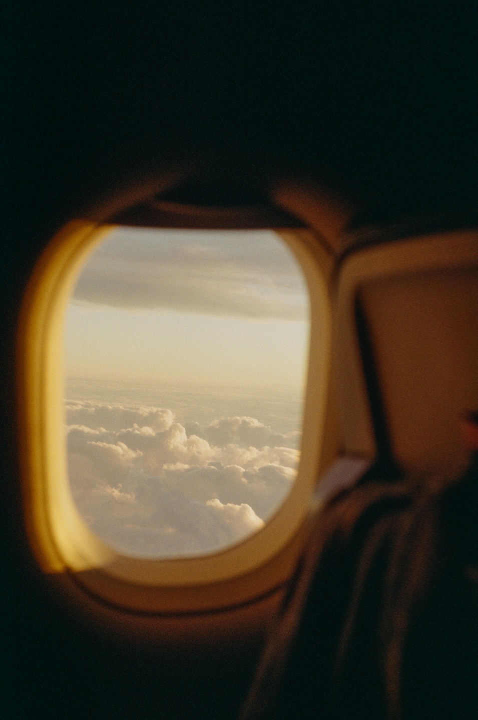 Clouds are visible through an airplane window during golden hour.
