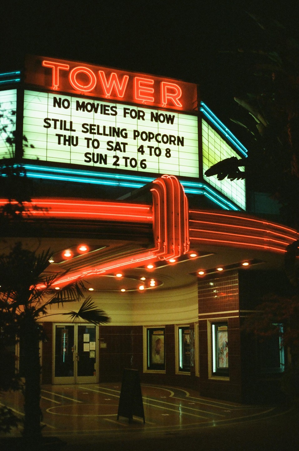 A movie theater marquee with neon lights advertises popcorn sales at night.